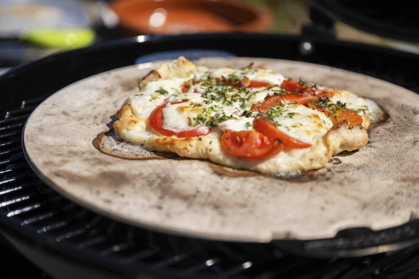 Pizza mit Tomaten, Käse und Kräutern auf dem Outdoorchef Pizzastein im Grill