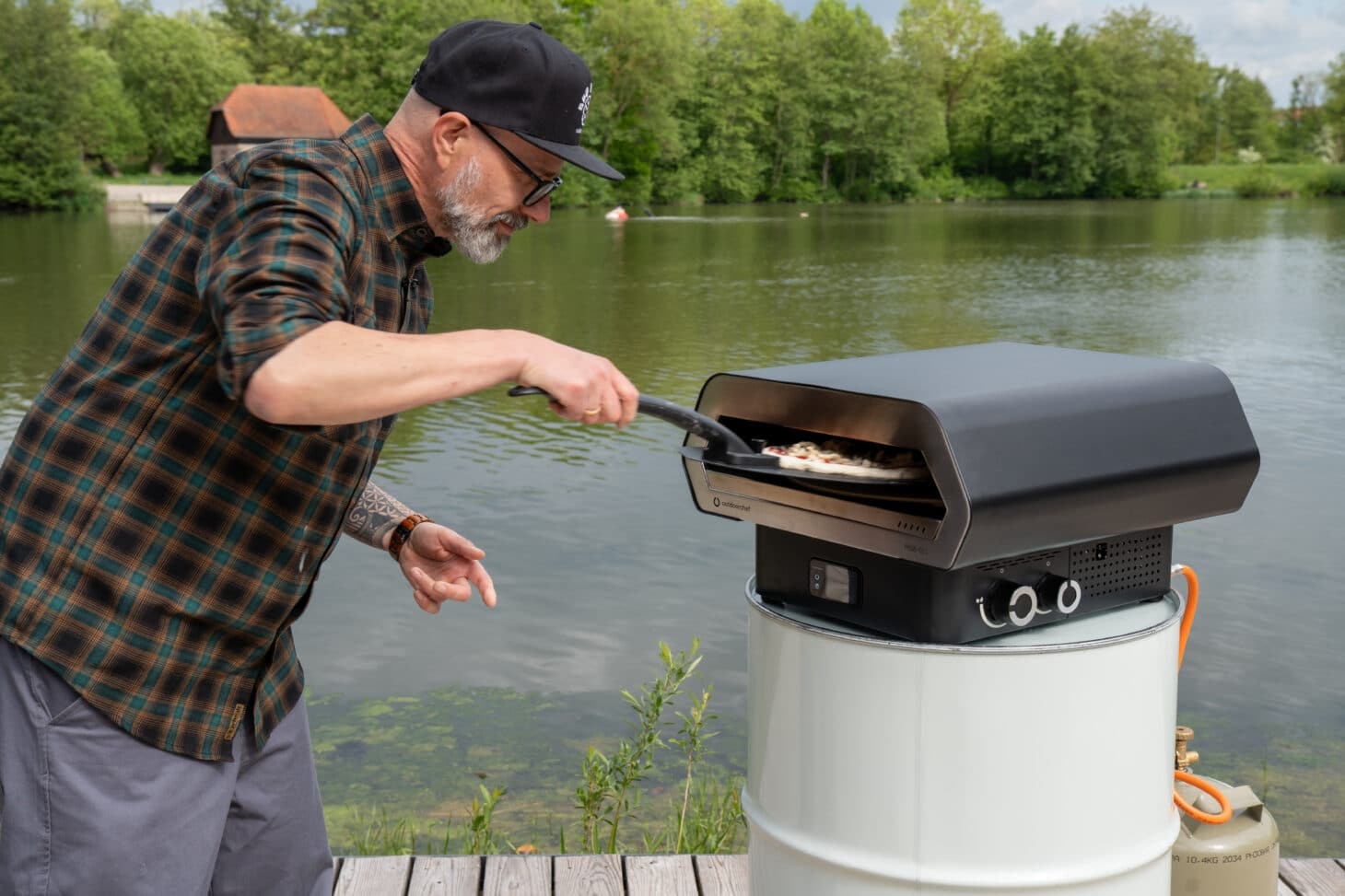 Outdoorchef PRISMO 420 G Pizzaofen mit Pizza auf der Pizzaschaufel am See