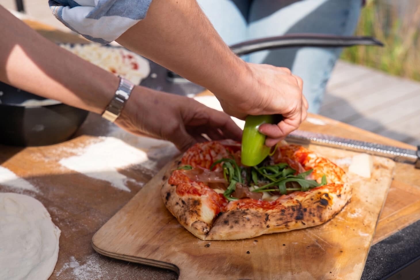 Pizzaschneider schneidet neapolitanische Pizza mit Rucola auf dem Pizzabrett